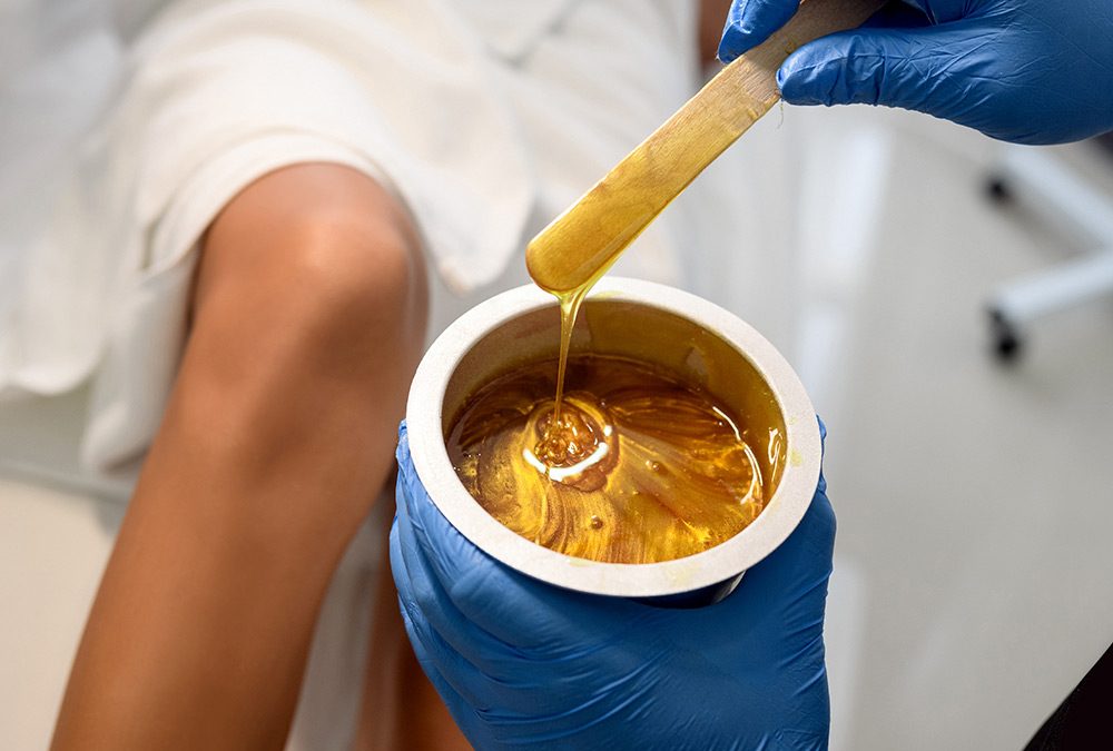 esthetician wearing gloves and stirring wax pot getting ready to wax someones leg for a blog about ingredients in hair wax